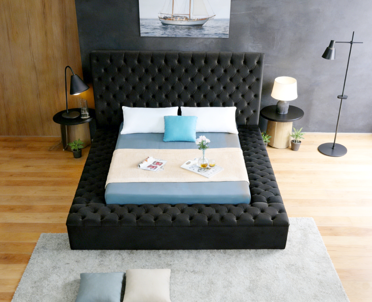 Modern bedroom with a tufted black bed, wooden floor, and wall art.