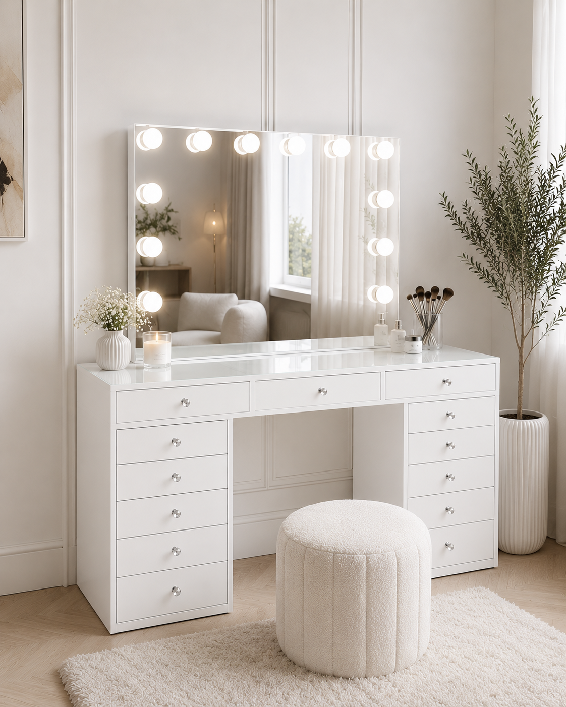 A white vanity table with a large lighted mirror, multiple drawers, and a round tufted ottoman in a bright, neutral-toned room.
